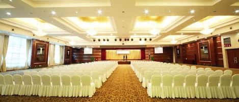 A conference room with rows of white chairs, a carpeted floor, and a stage with a podium.