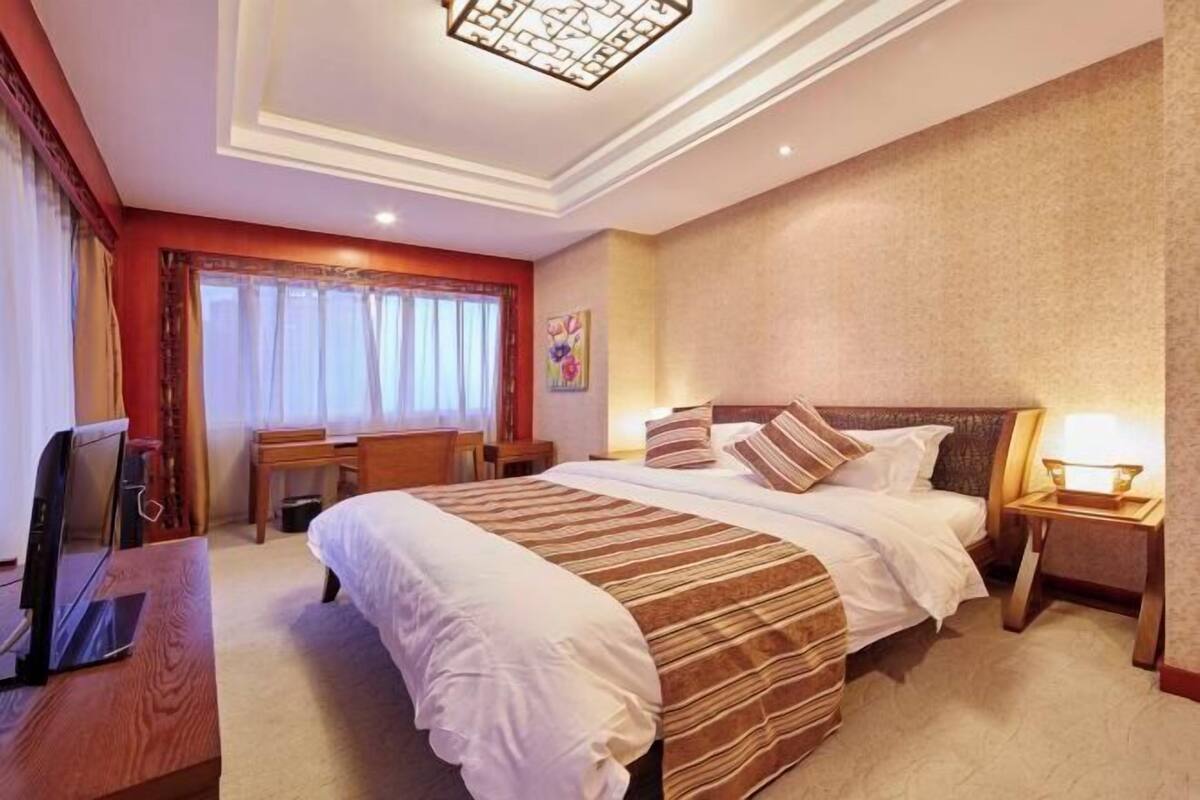 A hotel room with a large bed, bedside tables, a desk, and a television.