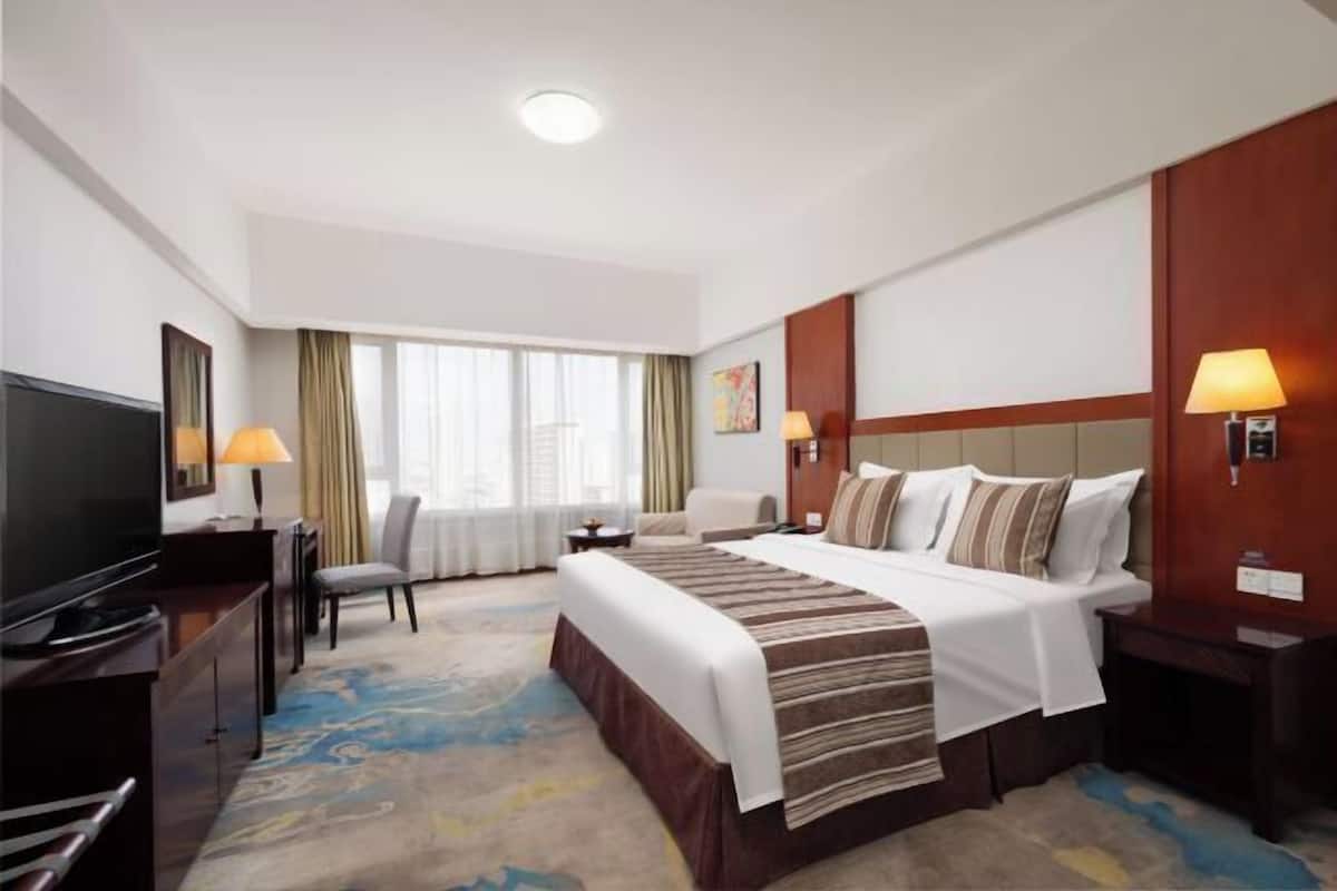 A hotel room with a bed, a TV, a desk, a chair, and a window with curtains.