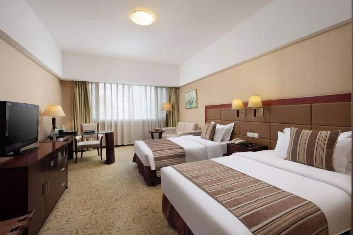 A hotel room with two beds, a TV, a desk with a chair, a lamp, and a painting on the wall.