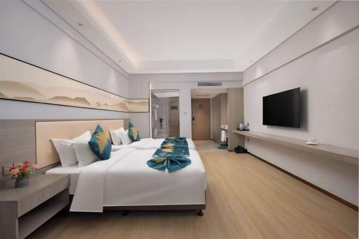 A modern hotel room with a large bed, a flat-screen TV, a bedside table, and a mirror on the wall.
