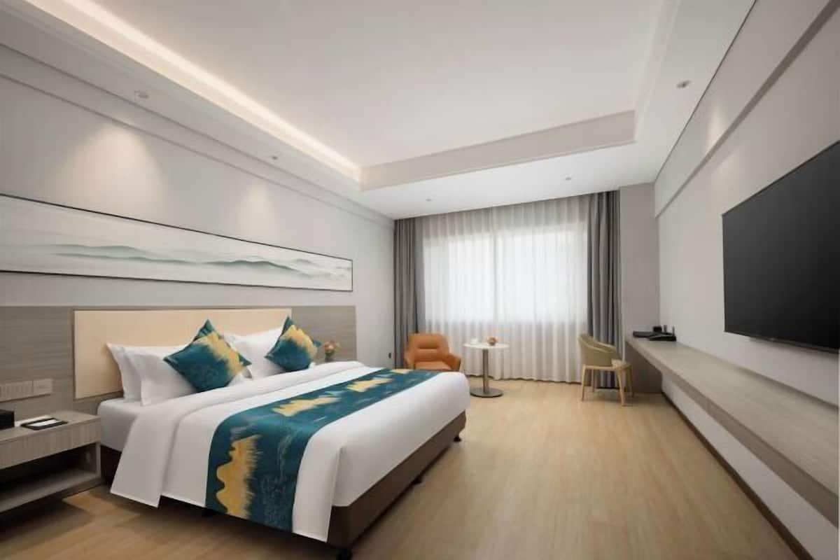A modern hotel room with a bed, a TV, a desk, and a chair.