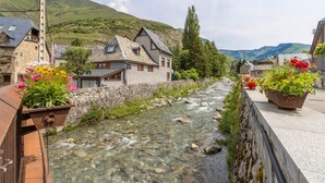 Ein Fluss fließt durch ein Dorf mit Steinhäusern und Blumenkästen.