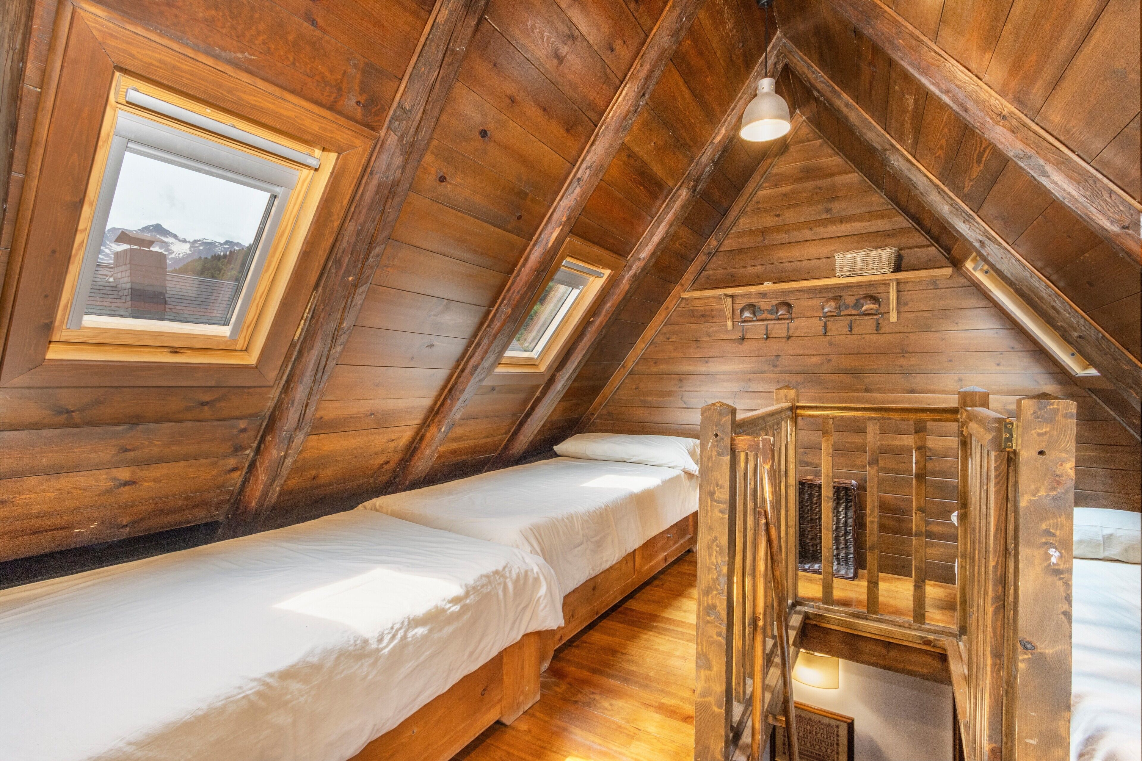 Ein Schlafzimmer im Dachgeschoss mit Holzboden, einem Schlafplatz auf Hochbett und Dachfenstern, erreichbar über eine Holzleiter.