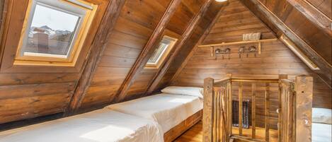 Ein Schlafzimmer im Dachgeschoss mit Holzboden, einem Schlafplatz auf Hochbett und Dachfenstern, erreichbar über eine Holzleiter.