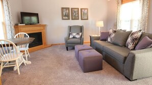 A living room with a fireplace, a television, a sofa, and a dining table with chairs. - Cottage with jacuzzi, Downtown Berlin Ohio (Berlin)