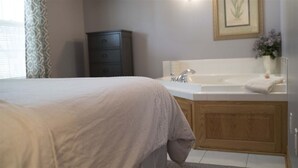 A bedroom with a bed, a wooden cabinet, a white bathtub, and a framed picture on the wall. - Cottage with jacuzzi, Downtown Berlin Ohio (Berlin)