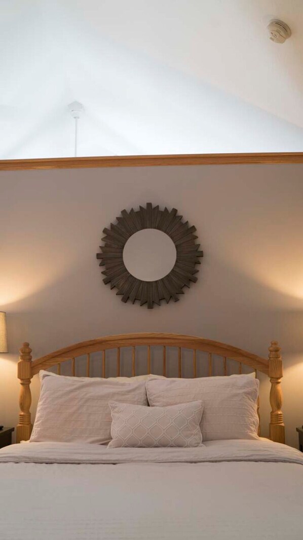 A bedroom with a wooden headboard, a round wall decoration, and two bedside lamps. - Cottage with jacuzzi, Downtown Berlin Ohio (Berlin)