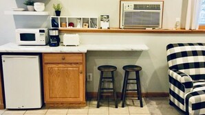 Une cuisine compacte équipée d’un four à micro-ondes, d’un grille-pain et d’un réfrigérateur. On y trouve deux tabourets et une chaise à motifs à carreaux.