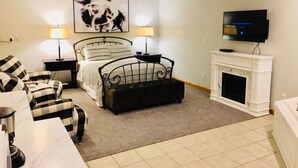 Une chambre à coucher comprenant un lit, deux tables de chevet avec des lampes, une télévision, une cheminée et un canapé.