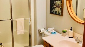 Une salle de bain avec une douche à parois de verre, des toilettes, un lavabo avec un miroir et une œuvre d’art encadrée au mur.