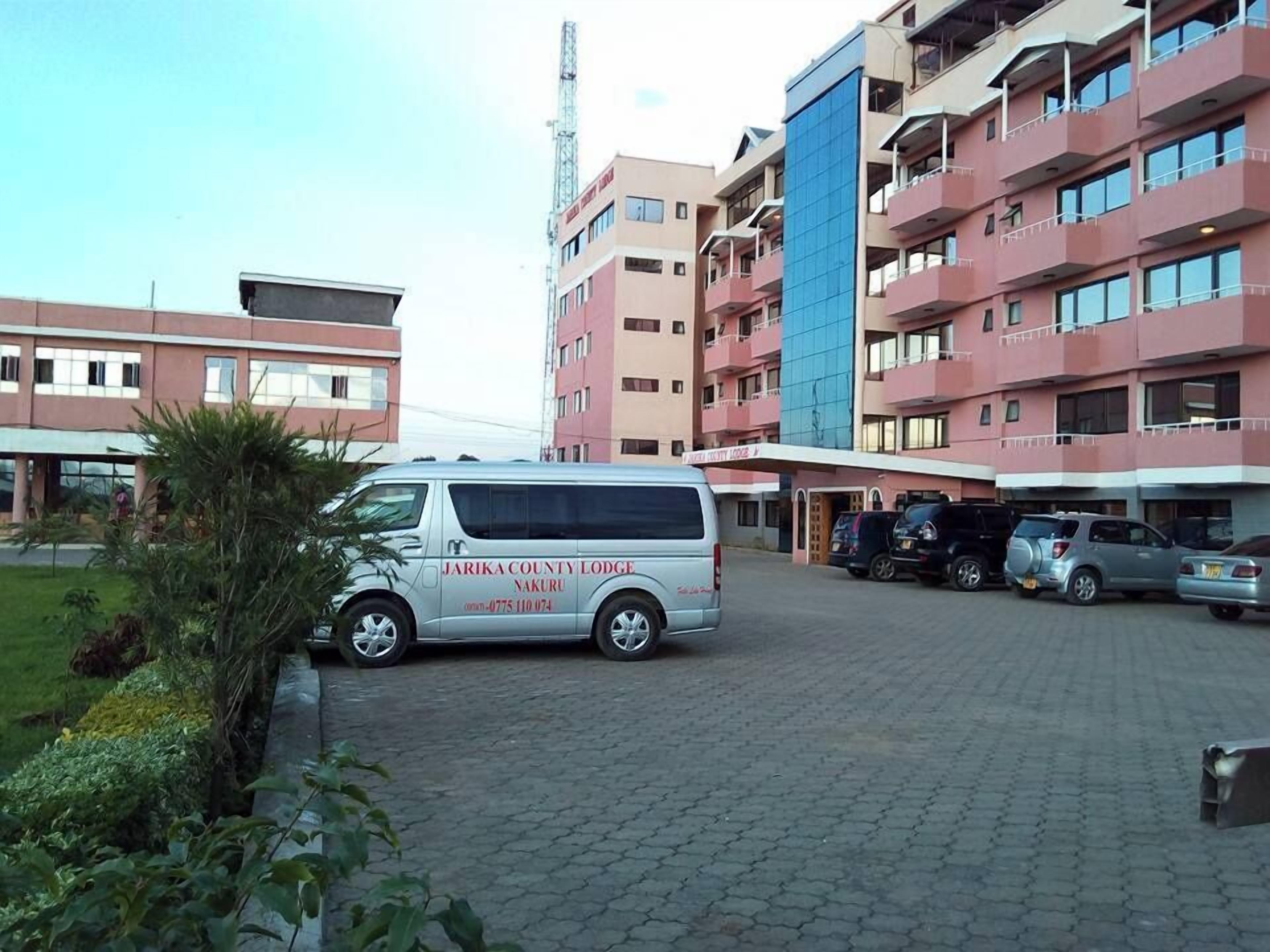 A multi-story building with a parking area. A white van is parked in front.
