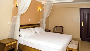 A neatly arranged bedroom with a bed, bedside tables, a chair, and a door. - Jarika Watamu Breeze Hotel (Nakuru)