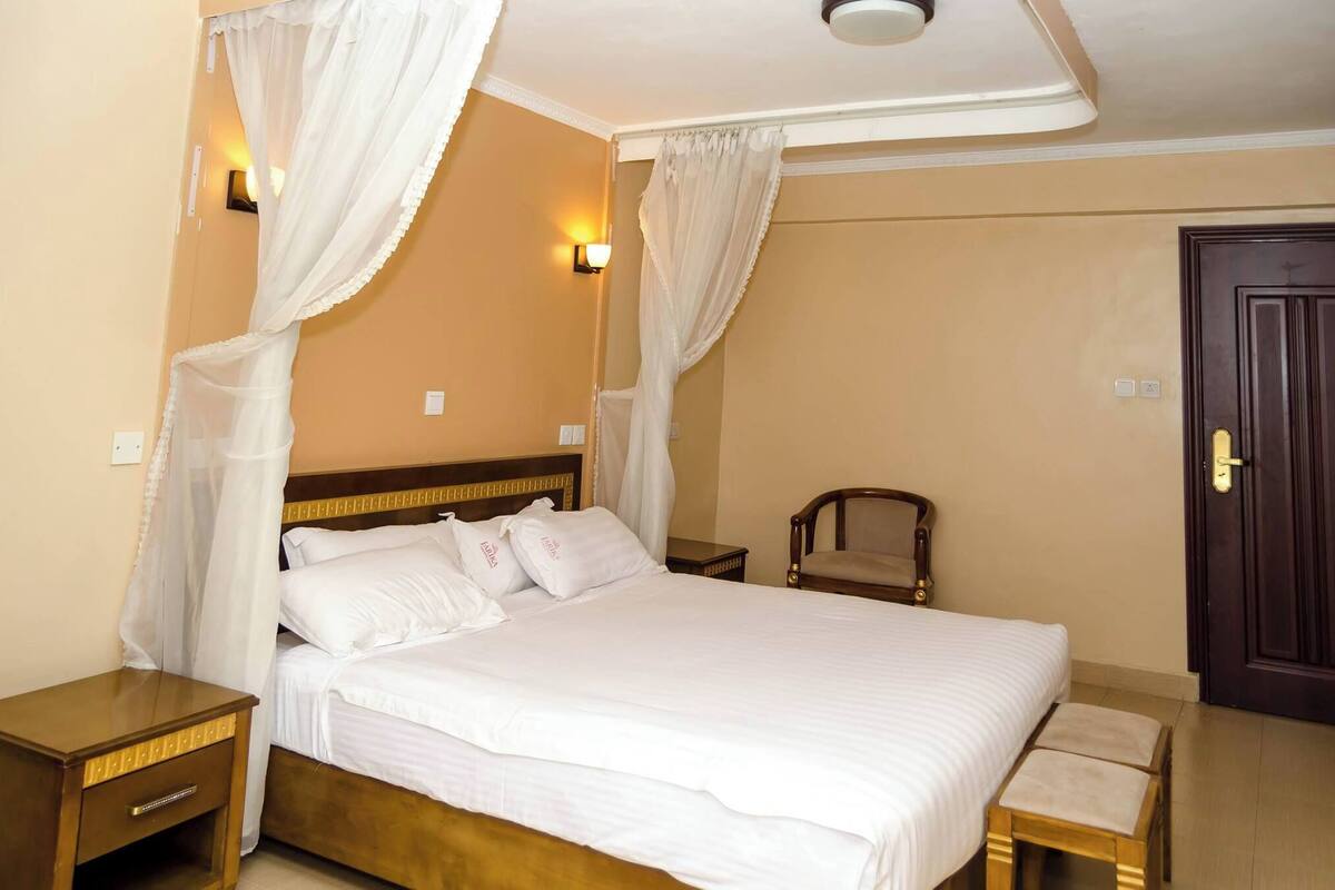 Un dormitorio ordenado con cama, mesitas de noche, una silla y una puerta.