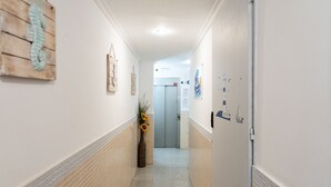 Un pasillo con suelo de baldosas, un adorno de pared de madera, un cuadro enmarcado y una puerta con un cartel.