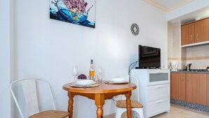 Un comedor con mesa de madera, dos sillas, un televisor y una cocina al fondo.