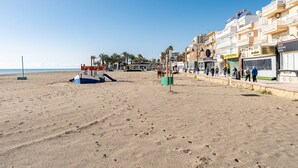 Una playa con una torre de salvavidas, palmeras y una hilera de tiendas, incluyendo un supermercado y una pizzería.