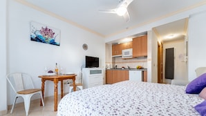 Un dormitorio con cama, escritorio, silla, televisor y kitchenette.
