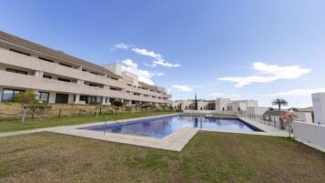 A modern building with a swimming pool, a fenced area, and a clear sky.