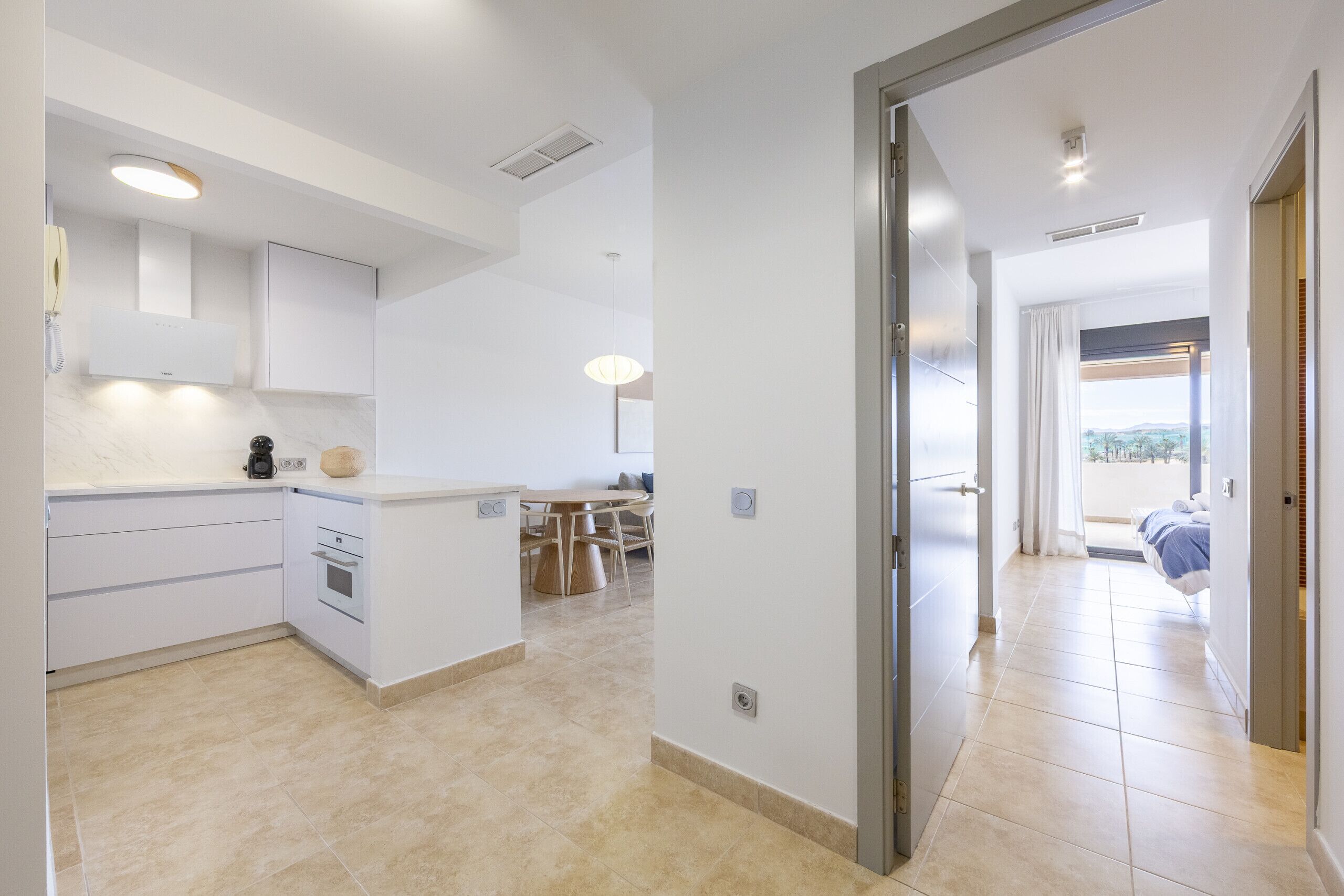 A modern kitchen with white cabinets, a built-in oven, and a dining area with a round table and chairs.