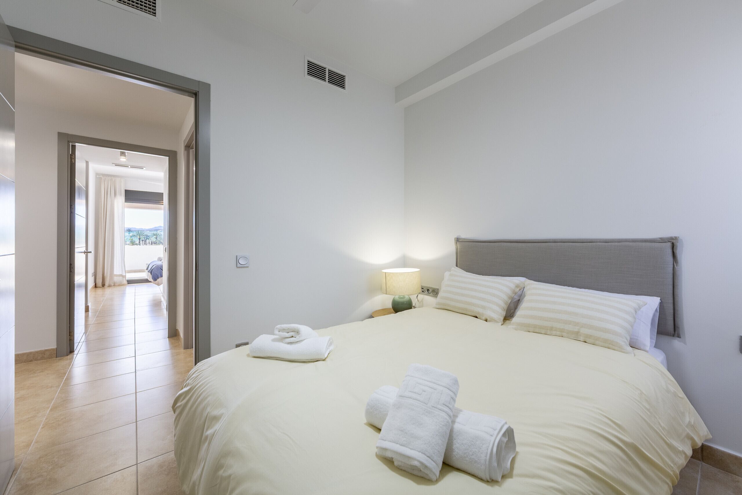 A hotel room with a bed, a nightstand, a lamp, and a view of a balcony.
