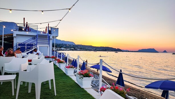 A seaside restaurant with outdoor seating, a staircase, and a view of the ocean at sunset. - Gorgeous home in Trabia (Trabia)