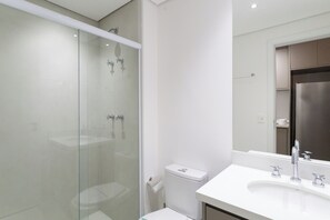 Un baño moderno con ducha de vidrio, lavamanos blanco y un espejo grande.