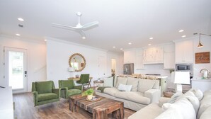 A modern living room with a sofa, chairs, a coffee table, and a kitchen area in the background. - Bridge View Retreat, Bridge View Retreat- Luxurious 4Br -Lake Martin Home (Alexander City)