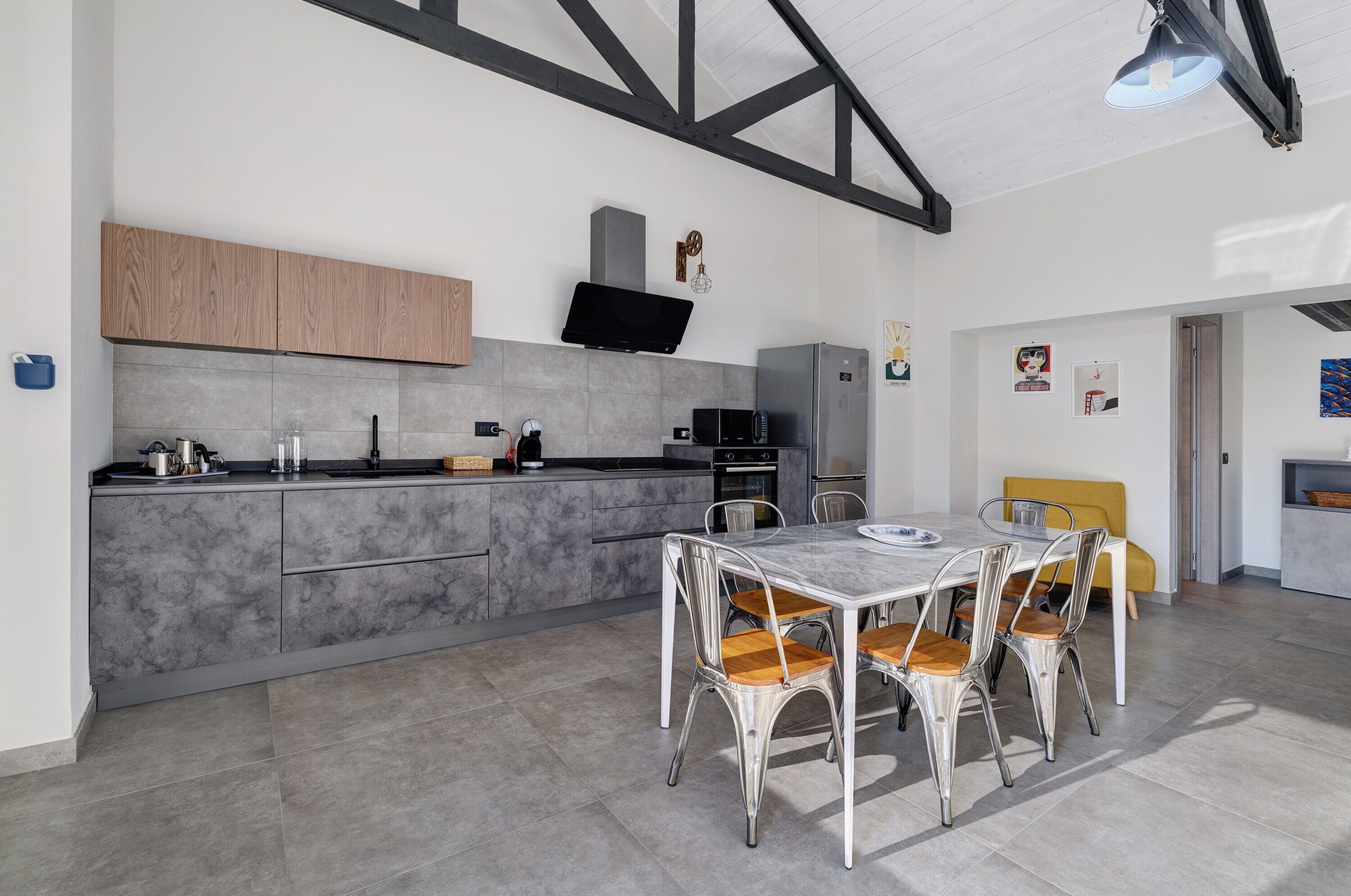 Une cuisine moderne avec des meubles gris, un micro-ondes encastré et un coin repas comprenant une table blanche et des chaises en métal.