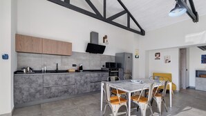 Una cocina moderna con armarios grises, microondas integrado y una zona de comedor con mesa blanca y sillas de metal.
