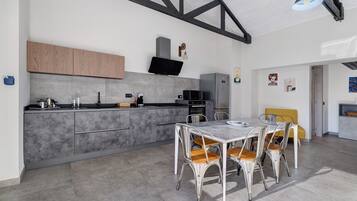 Une cuisine moderne avec des meubles gris, un micro-ondes encastré et un coin repas comprenant une table blanche et des chaises en métal.