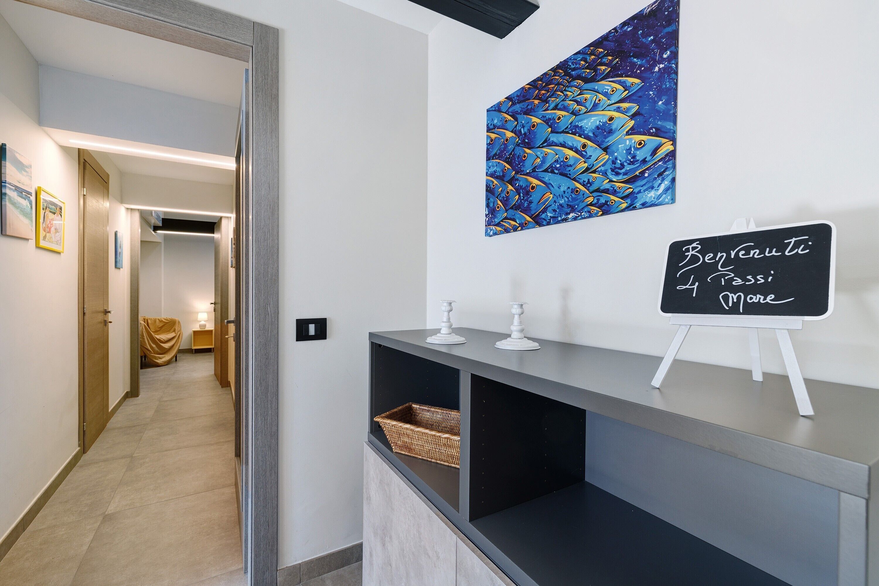 Un couloir avec un comptoir d’accueil, un tableau représentant des poissons accroché au mur et un panneau noir.