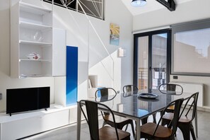 A modern dining area with a glass table, metal chairs, a flat-screen TV, and a staircase with a blue accent. - Apartment '4 Passi Mare 3' with Balcony, Wi-Fi and Air Conditioning (Finale Ligure)