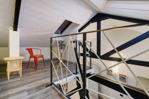 A modern interior with a wooden floor, a red chair, a small table, and a staircase with a metal railing. - Apartment '4 Passi Mare 3' with Balcony, Wi-Fi and Air Conditioning (Finale Ligure)