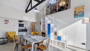 Un interior moderno con comedor, sillón amarillo, escalera y obras de arte en las paredes.