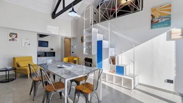 Un intérieur moderne comprenant un coin repas, un fauteuil jaune, un escalier et des œuvres d’art accrochées aux murs.