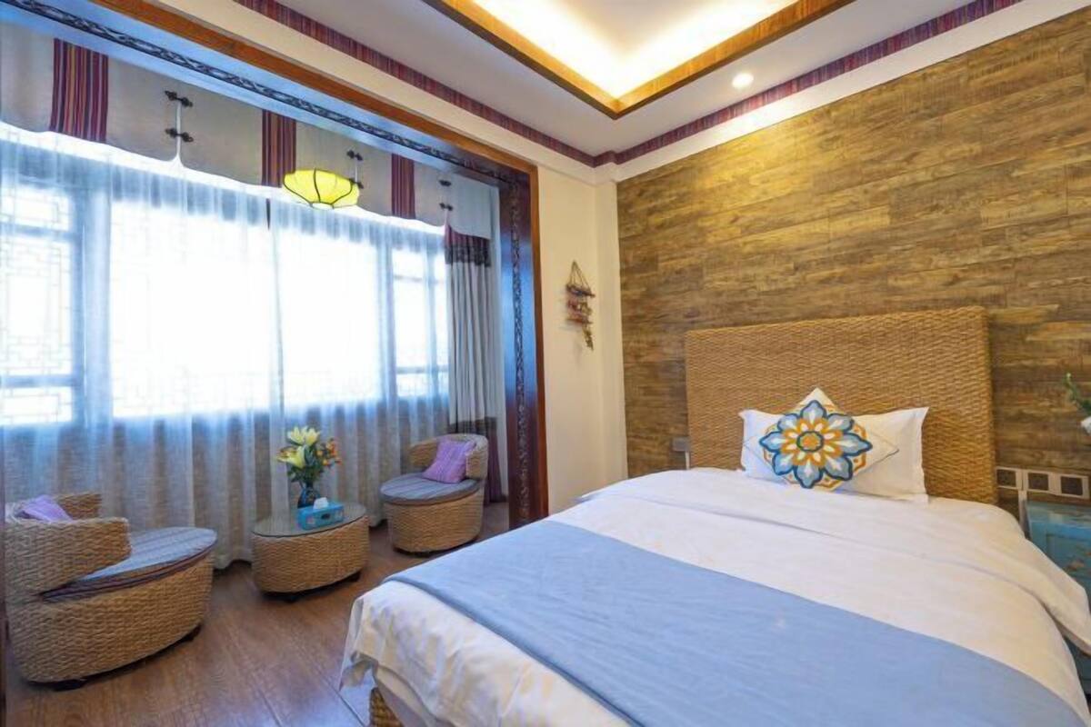 Ein Hotelzimmer mit einem großen Bett, zwei Korbstühlen, einem kleinen Tisch mit einer Vase und einer Wand mit Holzelementen.