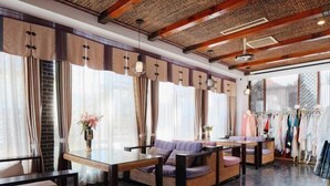 A modern interior with a high ceiling, exposed wooden beams, and large windows with curtains. There is a seating area with a table and chairs, and a clothing rack in the background. - Langyue Hanfu Travel Theme Inn (Lijiang Ancient City Branch) (Lijiang)