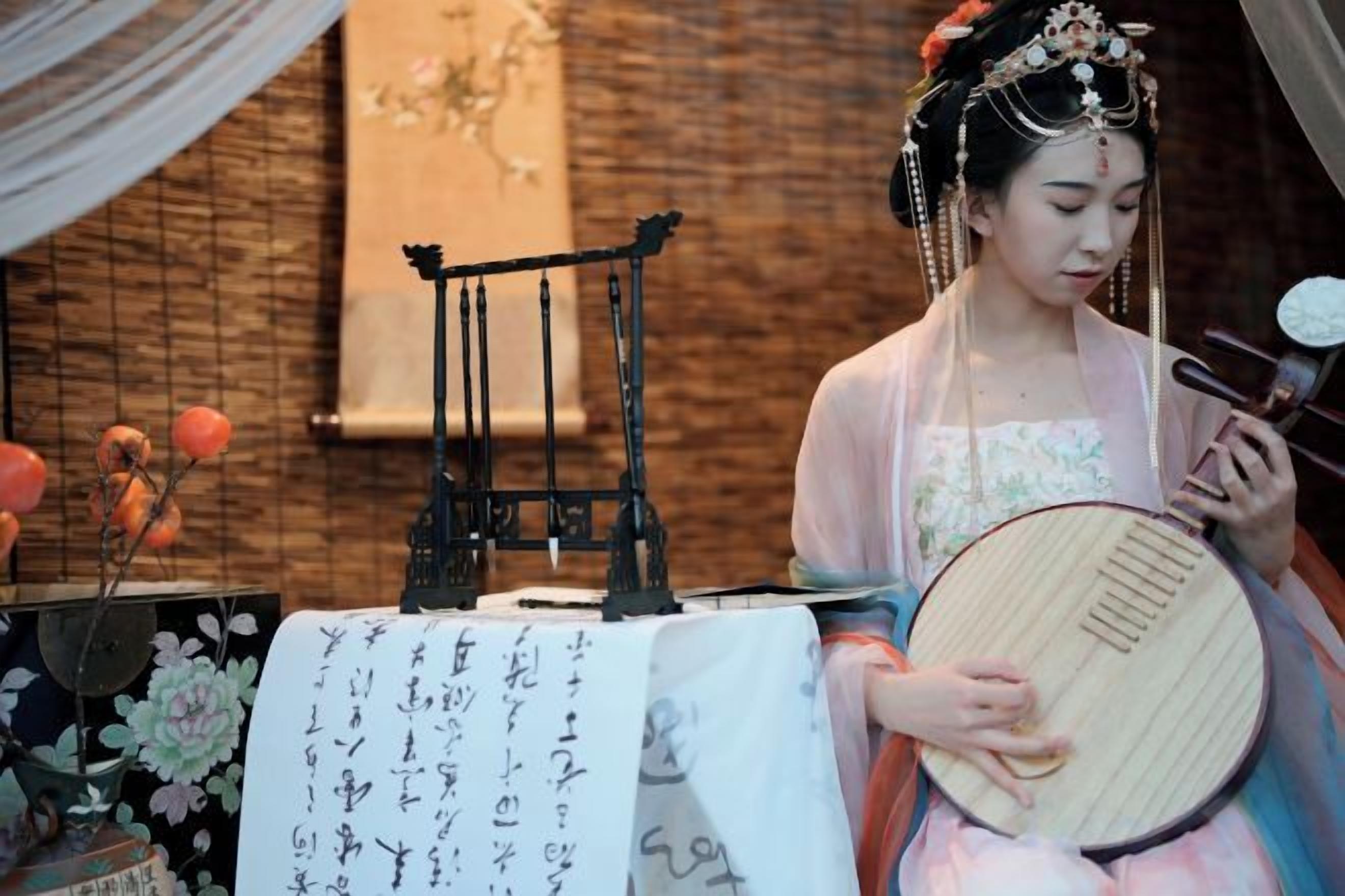 Una persona tocando un instrumento de cuerda tradicional, sentada a una mesa con un adorno y un papel con texto.