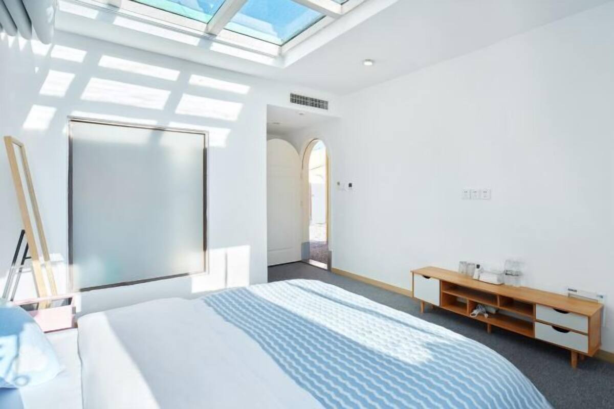 Ein modernes Hotelzimmer mit Dachfenster, einem Bett, einem Nachttisch aus Holz und Blick ins Freie.