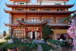 A traditional multi-story building with a prominent entrance, a garden with potted plants, and a decorative awning. - Langyue Hanfu Travel Theme Inn (Lijiang Ancient City Branch) (Lijiang)