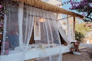 A traditional Japanese-style room with tatami flooring, a straw roof, and a serene garden view.