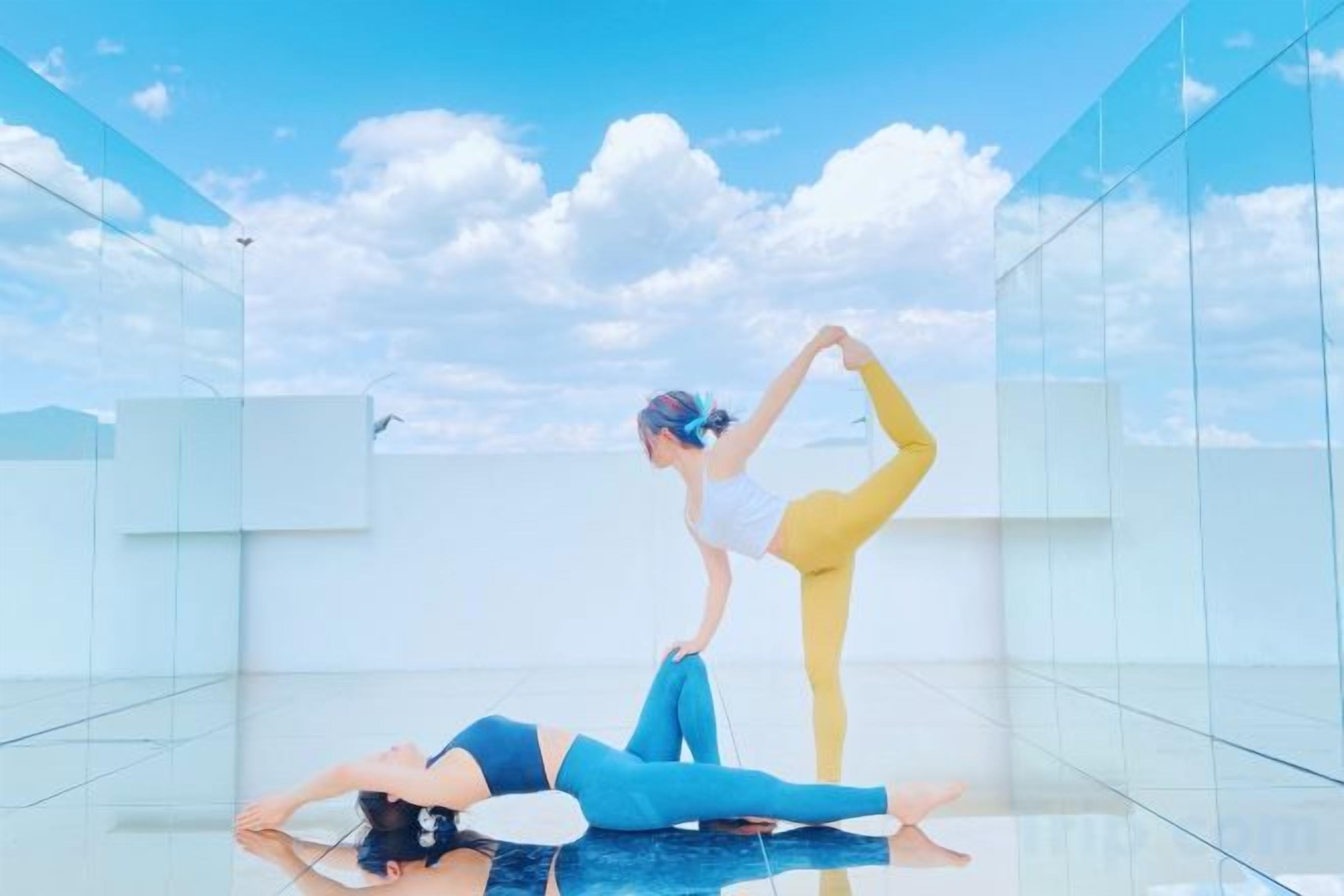 Two individuals performing yoga on a glass floor with a clear sky in the background.