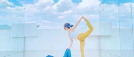 Two individuals performing yoga on a glass floor with a clear sky in the background.