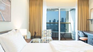 Habitación de hotel con cama, escritorio, silla y balcón con vistas a la ciudad.