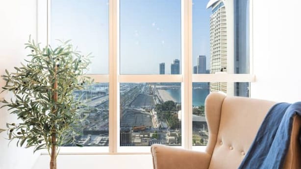 Una habitación con un amplio ventanal que ofrece vista a la ciudad, una planta en maceta y un sillón color beige.