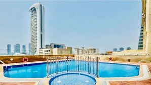 Una piscina en la azotea con un jacuzzi circular, rodeada por una barandilla metálica, y un paisaje urbano de fondo.