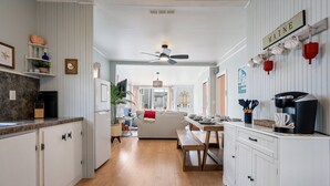 Una cocina con armarios blancos, encimera de madera, ventilador de techo y comedor con banco y mesa.
