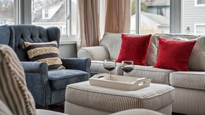 Un salón con un sillón azul, sofá a rayas y cojines rojos. Hay dos copas de vino sobre una bandeja.