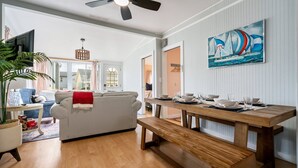 Una sala de estar moderna con un sofá, una mesa de comedor preparada para cuatro personas y un ventilador de techo.